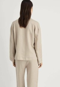 Beige linen sweater with a relaxed fit, drop shoulders, and simple stitching detail. Paired with matching linen pants, featuring a smooth texture.