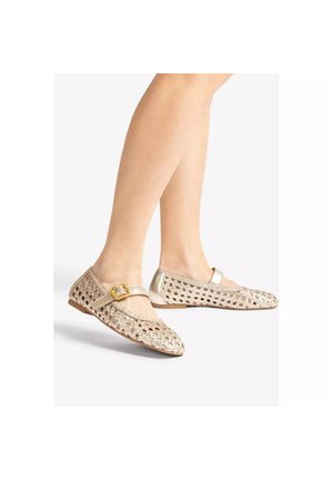 Ballerines Mary Jane tissées dorées avec bride à boucle portées aux pieds sur fond blanc.
