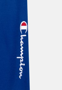 Blue cotton t-shirt with white embroidered "Champion" logo, featuring a red and white circular accent above the text.