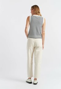 Top senza maniche a righe in blu navy e bianco, abbinato a pantaloni color crema. Il modello sta in piedi con le mani ai fianchi, mostrando la vista posteriore.