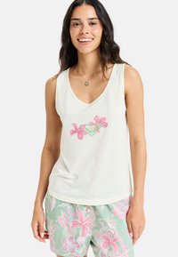 Weißes ärmelloses Oberteil mit V-Ausschnitt, das in der Mitte mit einem pinken Blumenmuster verziert ist. Weicher Stoff; lässige Passform. Kombiniert mit gemusterten Shorts.