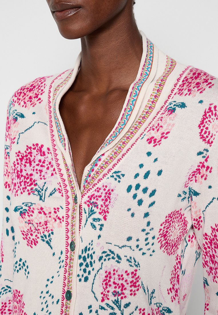 Gebreide cardigan met een bloemenpatroon in roze en teal op een crèmekleurige achtergrond, met een gestreepte kraag en groene knopen.