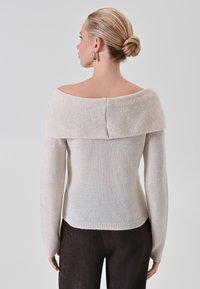 Maglione beige chiaro, scollato sulle spalle, con colletto a costine, maniche lunghe e una superficie liscia. Cucitura decorativa nella parte superiore della schiena.
