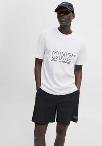 Hvid t-shirt med sort "CNZ" logo og tekst, parret med sorte shorts. Blødt bomuldsstof, afslappet pasform, minimalistisk design og uden mønstre.