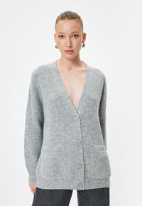Grå stickad cardigan med V-hals, två framsidor fickor och knäppning. Texturerad tyg med en mjuk, mysig look.