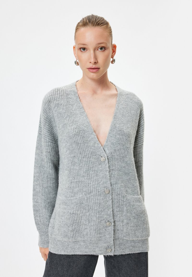 Grå stickad cardigan med V-hals, två framsidor fickor och knäppning. Texturerad tyg med en mjuk, mysig look.
