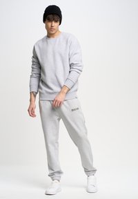 Lichtgrijze sweatshirt met ronde hals, gecombineerd met bijpassende tapersweatpants met een "BIG STAR" logo. Zwarte beanie en witte sneakers.