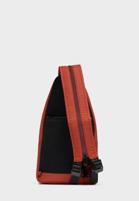 Slanke driehoekige slinger rugzak in roestoranje met zwart gaas achterpaneel en verstelbare schouderriem met gesp sluitingen.