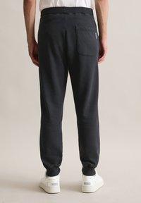 Dunkelgraue Sweatpants mit einer lockeren Passform, ausgestattet mit einer Gesäßtasche und gerippten Bündchen, kombiniert mit weißen Turnschuhen.