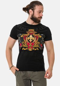 Schwarzes T-Shirt mit kurzen Ärmeln und Grafikdesign, das goldene, rote und gelbe Elemente, Pantherbilder und Markentext zeigt, aus Baumwollmaterial gefertigt.