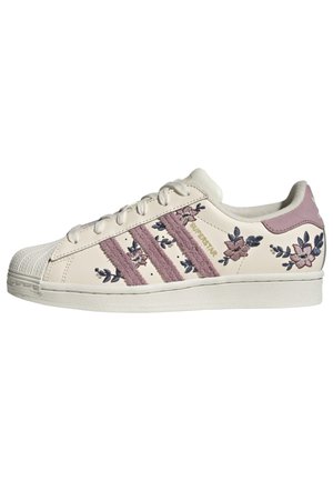 Hvid Adidas Superstar sneaker med lyserøde ruskindstriber og lyserødt og blåt blomsterbroderi langs siderne og på hælskinnen.