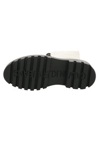 Suela de goma negra con ranuras profundas para tracción, con texto en relieve "CALVIN KLEIN JEANS." Parte superior lisa y de color claro visible arriba.