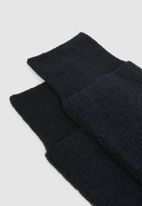 Schwarze Socken mit einem strukturierten, Frottee-Design. Verfügt über einen gerippten Bund und eine glatte Unterseite, die ein weiches und komfortables Erscheinungsbild bieten.