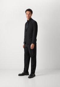 Black suit made of smooth fabric, featuring a single-button blazer and tailored trousers, paired with glossy black dress shoes.