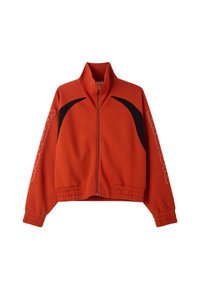 Giacca arancione ruggine con zip, dettagli neri curvi sulle spalle, polsini e orlo elasticizzati, e testo del logo discreto sulle maniche.