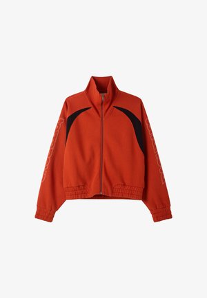 Giacca arancione ruggine con zip, dettagli neri curvi sulle spalle, polsini e orlo elasticizzati, e testo del logo discreto sulle maniche.