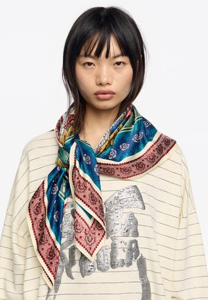 Foulard di seta con motivi intricati nei toni del blu, rosso e oro, annodato attorno al collo, con una texture liscia e una forma quadrata.