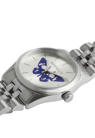 Strieborné hodinky z nerezovej ocele s motívom motýľa v modrej farbe na bielej ciferníku. Obsahujú lesklé puzdro a náramok s článkami. Aktívny detail korunky.