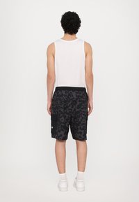 Svarte cargo-shorts med leopardmønster, elastisk linning og sidelommer, kombinert med en hvit tanktop og hvite sneakers.