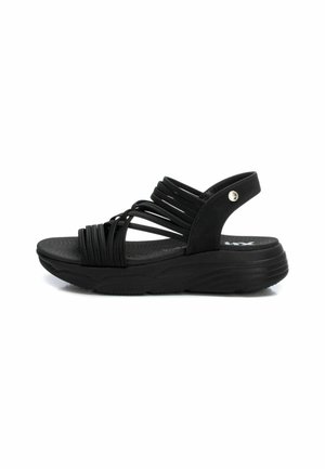 Sandalia negra con suela de goma texturizada, que presenta múltiples correas elásticas en la parte frontal y una correa trasera de soporte.