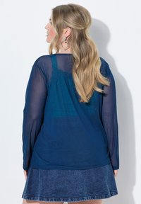 Mörkblå genomskinlig blus med långa ärmar och spetsdetaljer, i kombination med en blå denimkjol. Blusen har en avslappnad passform.