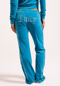 Türaquoise Velour-Sweatpants mit lockerer Passform, ausgestattet mit glitzerndem "Juicy"-Schriftzug auf der Rückseite, glatter Textur und elastischem Bund.