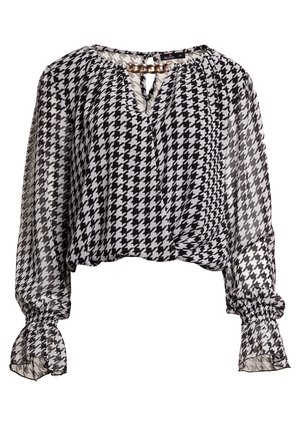 Schwarz-weiße Bluse im Hahnentrittmuster, cropped, mit transparenten langen Ärmeln, elastischen Bündchen und einem Kettenakzent am Ausschnitt.