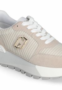 Sneaker beige clair avec une tige en maille texturée, des accents en suède et des lacets blancs. Dispose d'un détail de logo doré et d'une semelle en caoutchouc gris épaisse.