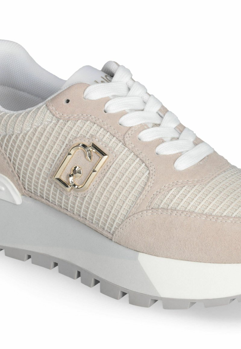 Helle beigen Sneakers mit strukturiertem Mesh-Obermaterial, Wildleder-Details und weißen Schnürsenkeln. Mit einem goldenen Logo-Detail und einer dicken grauen Gummisohle.