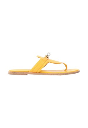 Gul flad sandal med tå-loop og en justerbar rem med en lille metalring over fodens svang.