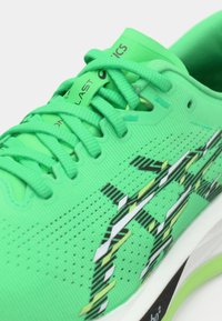 Chaussure de sport vert vif avec lacets assortis, logo noir et jaune à motif sur le côté, et semelle blanche avec des touches noires et vertes.