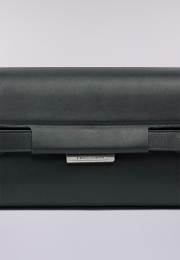 Clutch in pelle nera dal design elegante, con chiusura magnetica e una placca con logo metallico. Texture liscia con accenti minimi.