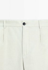 Pantalon beige clair en tissu texturé, doté d'un bouton noir, de passants de ceinture et d'un design de poche avant classique.