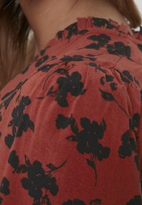 Gros plan sur un tissu rouge avec des motifs floraux noirs sur une épaule froncée et un décolleté volé d'un vêtement.