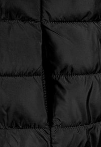 Giacca a vento nera con design trapuntato, texture lucida e liscia, dettagli cuciti e zip nascosta sul davanti.
