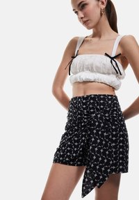 Biały, teksturowany crop top z czarnymi ramiączkami w zestawieniu z czarnymi szortami z kwiatowym wzorem i zwiewnym krojem.