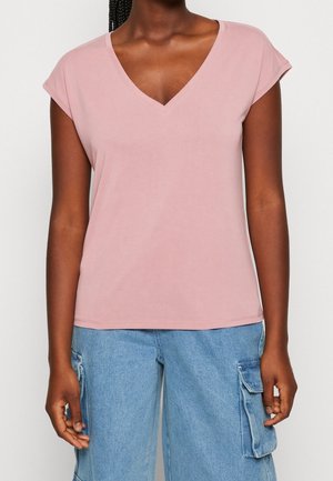 Woman wearing a light pink V-neck short sleeve top and light blue denim cargo pants, shown from shoulders to hips.