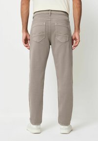 Bežid sirgedega teksad s suju tekstuuriga, millel on kaks tagataskut ja peened õmblused. Kombineeritud valgete tossudega.