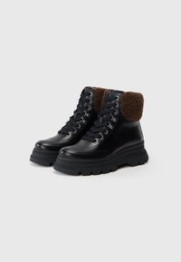 Botas con suela gruesa negra y cordones, con forro de felpa marrón en el puño, adecuadas para el clima frío, exhibidas sobre un fondo blanco liso.