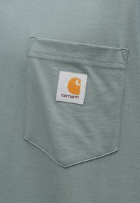 Ανοιχτό μπλε κοντομάνικο μπλουζάκι με τσέπη στο στήθος που έχει ένα τετράγ ωνο λευκό έμβλημα και ένα πορτοκαλί λογότυπο. Απαλή υφή και απλός σχεδιασμός.