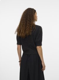 Pull à manches courtes, gris foncé, en tricot avec un tissu texturé et un ourlet côtelé, associé à une jupe noire fluide. Les cheveux bouclés du mannequin tombent aux épaules.