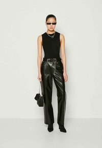 Canotta nera abbinata a pantaloni in pelle sintetica nera a vita alta. Presenta una cintura in catena argentata e accessori neri eleganti.