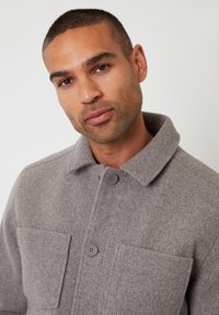 Szary, wełniany żakiet w połączeniu z innymi włóknami, z kołnierzem, zapięciem na guziki z przodu i dwiema kieszeniami naszytymi. Teksturalna tkanina o miękkim wyglądzie.