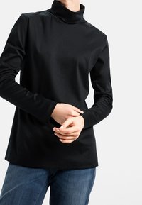 Schwarzes Langarm-Turtleneck aus glattem Stoff, mit taillierter Passform und schlichter Silhouette, kombiniert mit Jeans.