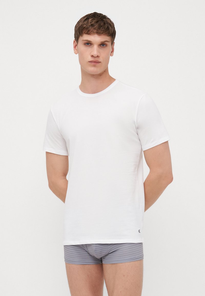 T-shirt en coton blanc avec un col rond et des manches courtes, assorti à un caleçon rayé gris et blanc. Design simple, texture lisse.