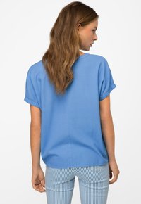 Top azzurro chiaro a maniche corte con risvolti, scollo rotondo e dettaglio di cucitura sul retro. Abbinato a pantaloni a righe verticali blu e bianchi.