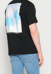 Černé bavlněné tričko s barevným grafickým motivem palmy na zadní straně, s pohodlným střihem a krátkými rukávy.