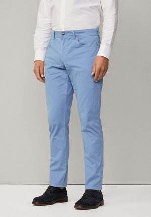Chinos bleu clair avec une coupe ajustée, en tissu de coton. Dotés d'une fermeture à bouton et de poches avant. Associés à des chaussures foncées.