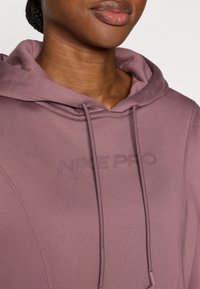 Nike Pro hoodie in gedempte paarse kleur, voorzien van een gestructureerde stof, een capuchon met trekkoorden en een geperst logodetail op de borst.