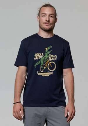 Marineblauw katoenen t-shirt met een afbeelding van een dinosaurus op een fiets, met de tekst "Fiets" en "Heb Plezier." Klassieke ronde hals.